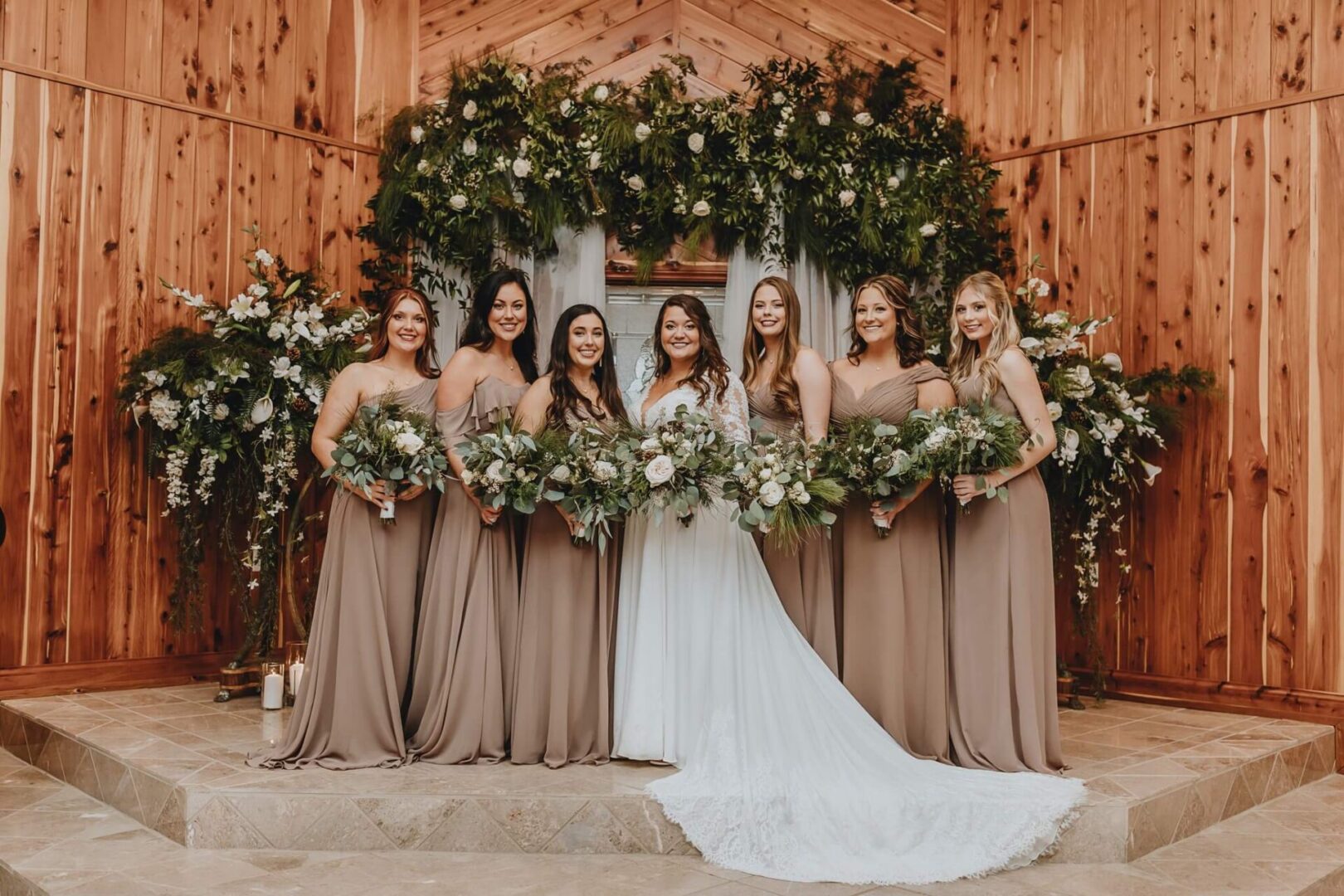 The bride and her bridesmaids pose in front of a wooden barn, with electric car chargers visible in the background.